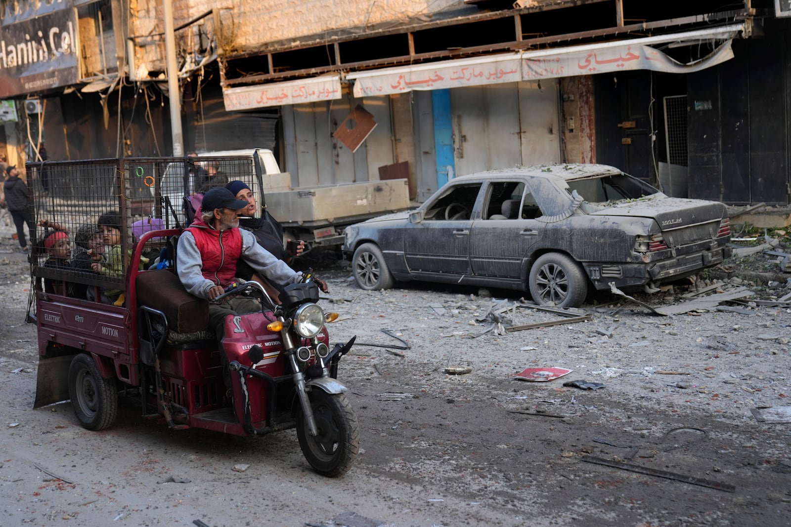 A man rides with his family a three-wheeled motorized known as "tok-toks," as they pass by a car that was damaged after an Israeli airstrike hit a building on Dahiyeh, in the southern suburb of Beirut, Lebanon, Friday, Nov. 1, 2024. (AP Photo/Hussein Malla)