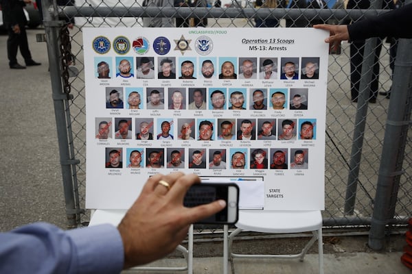 A reporter uses his telephone to photograph a poster showing suspected members of MS-13 in Los Angeles in 2017. ASSOCIATED PRESS