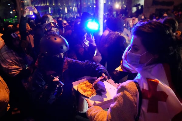 A woman distributes pizza to demonstrators during a rally outside the parliament's building to protests against the government's decision to suspend negotiations on joining the European Union, in Tbilisi, Georgia, Wednesday, Dec. 4, 2024. (AP Photo/Pavel Bednyakov)