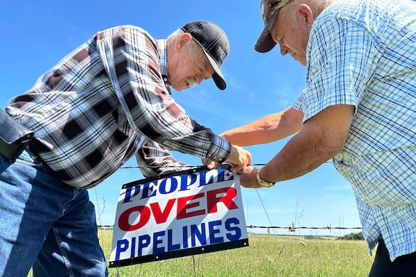 FILE - Gaylen Dewing, left, and Marvin Abraham affix a sign to a roadside fence east of Bismarck, N.D., Tuesday, Aug. 15, 2023, in opposition to Summit Carbon Solutions' proposed five-state, 2,000-mile pipeline network to carry carbon dioxide emissions from dozens of Midwestern ethanol plants to North Dakota for permanent storage deep underground. (AP Photo/Jack Dura, File)