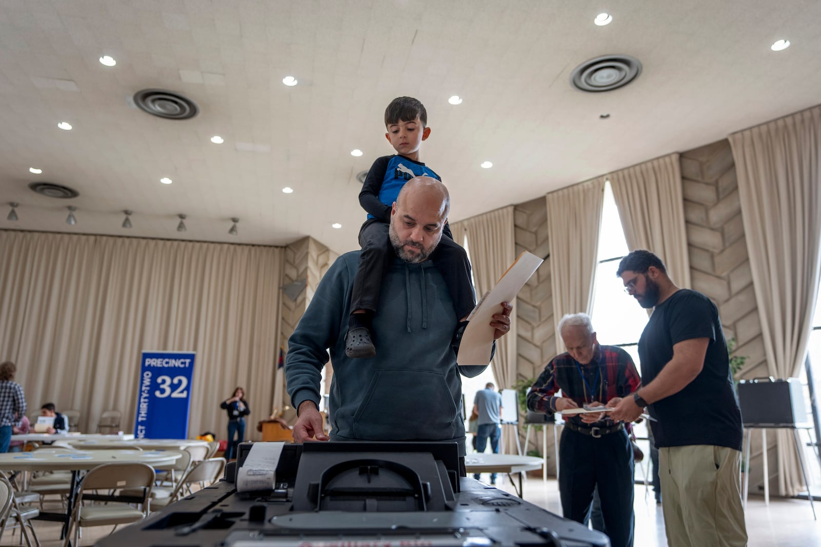 Three-year-old Zayn, sits on his father's shoulders as he inserts his ballot into a machine to vote at the First Presbyterian Church of Dearborn, on Election Day, Tuesday, Nov. 5, 2024, in Dearborn, Mich. (AP Photo/David Goldman)