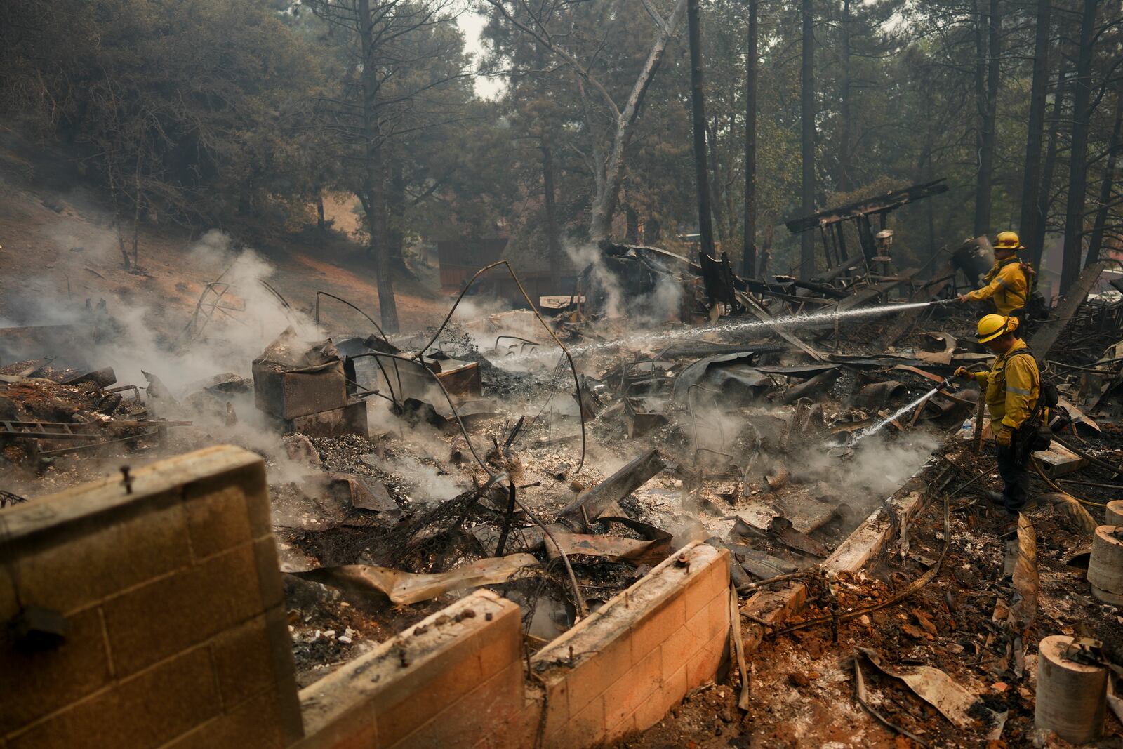 Firefighters hose down hot spots on a fire-ravaged property while battling the Bridge Fire Wednesday, Sept. 11, 2024, in Wrightwood, Calif. (AP Photo/Eric Thayer)