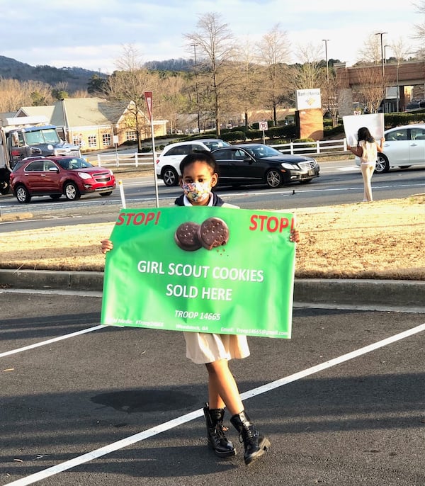 Lundyn Samuel (in the foreground) and Gabbi Groce (upper right) hold signs to lure shoppers to their troop’s drive-through cookie booth. Courtesy of Michele Samuel