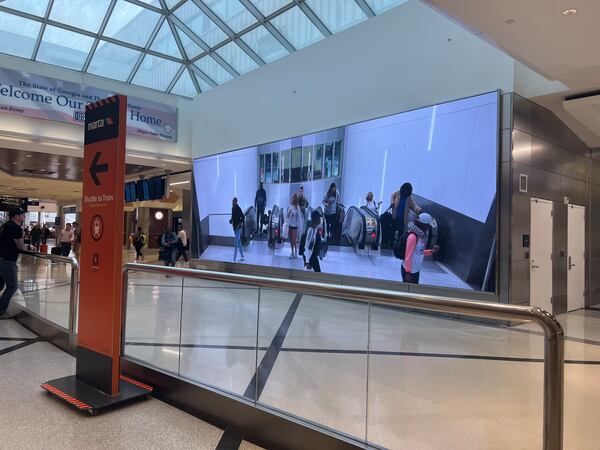 A video screen shows arriving passengers at the top of the escalators at at Hartsfield-Jackson International Airport.