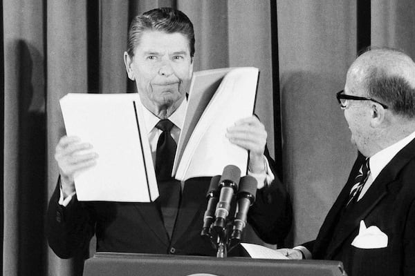 FILE - President Ronald Reagan displays reports given to him by J. Peter Grace, right, of the Private Sector Survey on Waste and Cost Control in Government, at the White House in Washington, Jan 16, 1984. (AP Photo/Ira Schwarz, File)