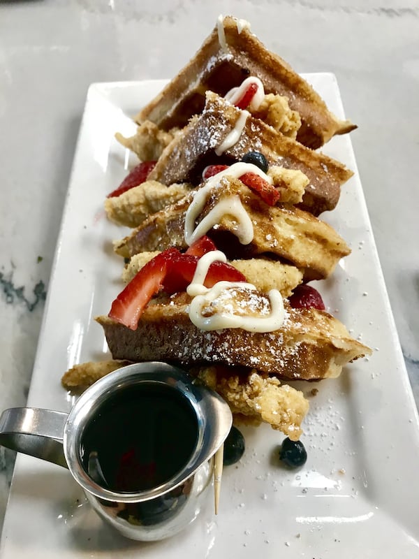 Topped with powdered sugar and a drizzle of vanilla sauce, the Chicken and Waffle Stack from Gocha’s Breakfast Bar is sweet enough even before pouring on the house-made bourbon maple syrup. LIGAYA FIGUERAS / LFIGUERAS@AJC.COM