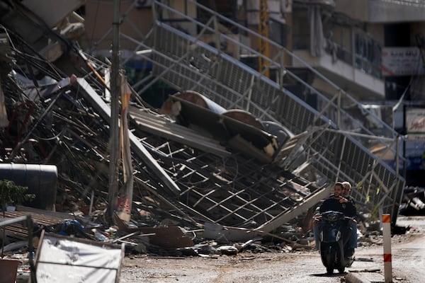 Two men ride a scooter past a building that was destroyed by an Israeli airstrike in Dahiyeh, in the southern suburb of Beirut, Lebanon, Monday, Nov. 11, 2024. (AP Photo/Hussein Malla)