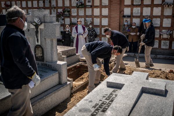 A priest and relatives pray as a victim of the COVID-19 coronavirus is buried by undertakers at the Almudena cemetery in Madrid.