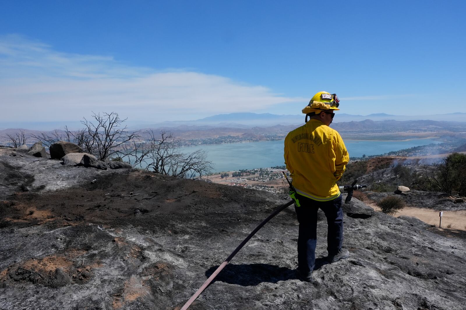 A Riverside County Fire Dept. firefighter monitors for hot spots overlooking Lake Elsinore after the Airport Fire swept through Wednesday, Sept. 11, 2024, in El Cariso Village, in unincorporated Riverside, County, Calif. (AP Photo/Gregory Bull)