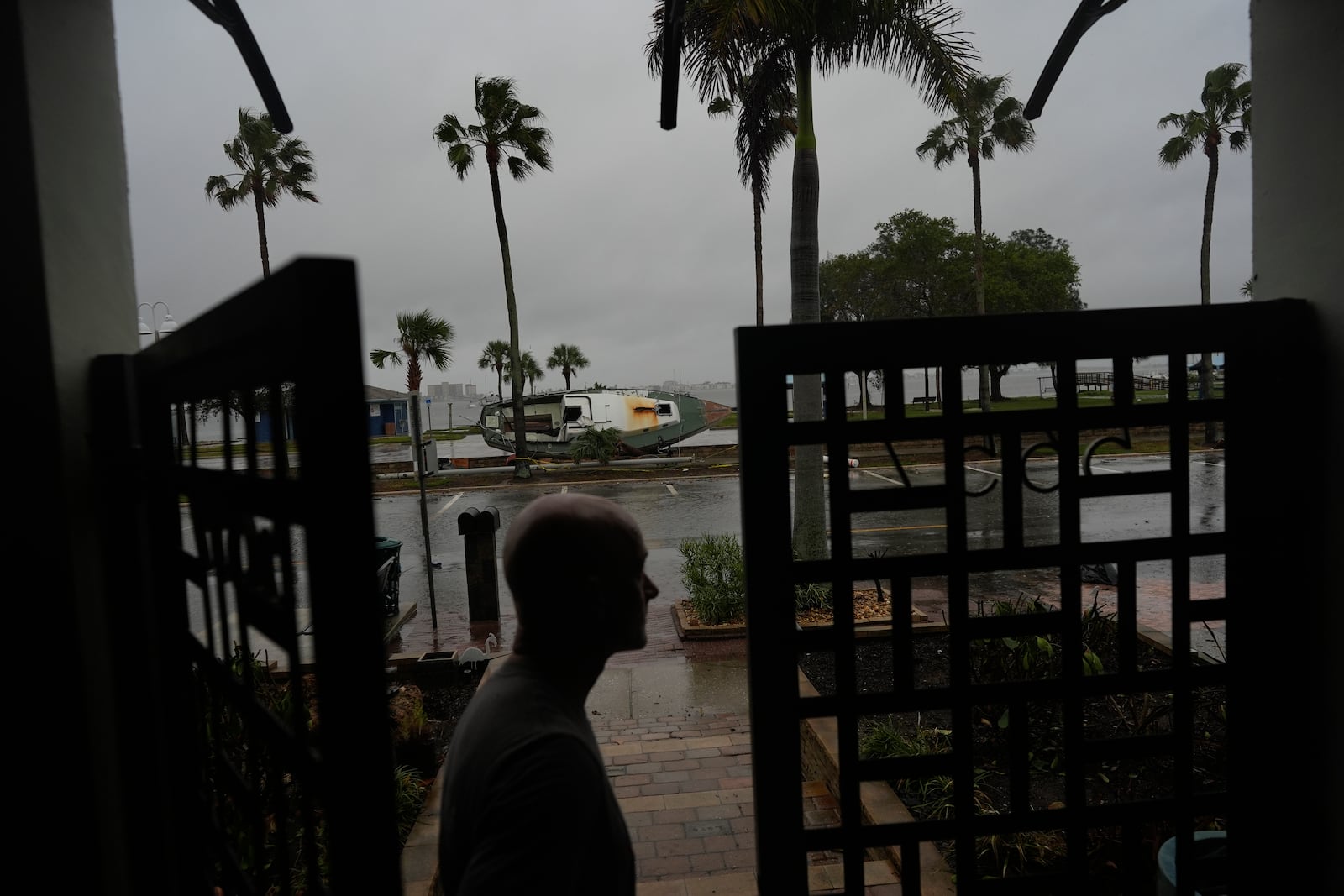 Christian Burke stands at the door of his home, where he, his mother, and his aunt plan to ride out Hurricane Milton on the third floor overlooking overlooking Tampa Bay, in Gulfport, Fla., Wednesday, Oct. 9, 2024. Burke, who said his engineer father built the concrete home to withstand a Category 5 hurricane, expects his raised ground floor to get up to 8 feet of water in Milton. A boat deposited by Hurricane Helene sits lodged in the bayfront park outside his front door. (AP Photo/Rebecca Blackwell)