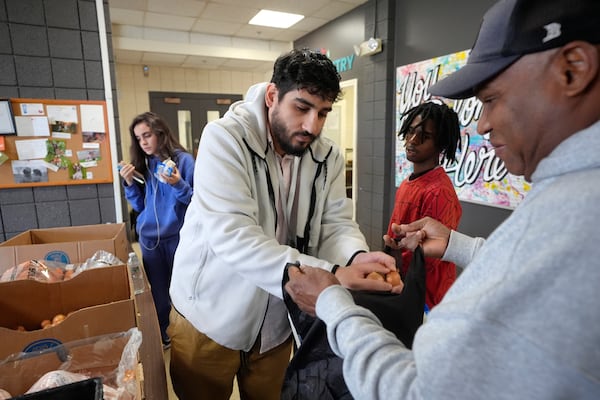 Volunteer Charles Mena, of Providence, R.I. center, places food in a bag for customer Hungria Hernandez Diomedes, right, in a food pantry at Federal Hill House, Tuesday, Nov. 12, 2024, in Providence, R.I. (AP Photo/Steven Senne)