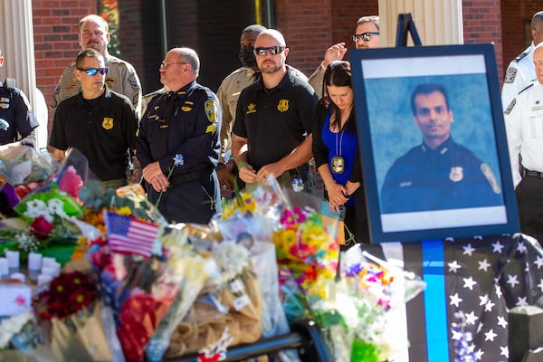 Police officers surround a cruiser covered with flowers during a prayer vigil for Officer Paramhans Desai on Friday.