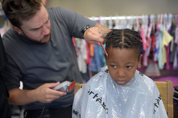 Matthew Miller, of Matthew’s & Co. Salon in Flowery Branch, works on Taishan Henderson, 8, on Monday. Miller brought 22 local stylists and assistants to give more than 100 free haircuts on Monday to get kids ready for school. It was a partnership with North Gwinnett Co-op, which helps families in need. KENT D. JOHNSON / KDJOHNSON@AJC.COM