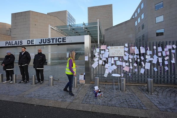 A woman walks past poster attached on the fence of the Palace of Justice during a women's rights demonstration, Saturday, Dec. 14, 2024 in Avignon, southern France, where the trial of dozens of men accused of raping Gisèle Pelicot while she was drugged and rendered unconscious by her husband is taking place. (AP Photo/Aurelien Morissard)