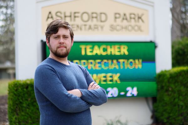 Third-grade teacher Brandon Wyatt poses in front of the school sign at Ashford Park Elementary on Wednesday, March 21, 2023. During his first year of teaching, Wyatt has faced challenges that make his job difficult. "Even though I enjoy teaching the kids, I don't plan to return next year," Wyatt said. (Miguel Martinez /miguel.martinezjimenez@ajc.com.)