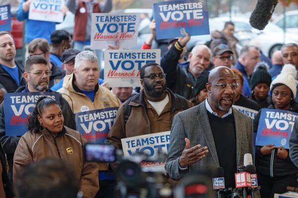 Sen. Raphael Warnock speaks to the media as Teamster UPS workers look on at the UPS Smart Hub facility in Atlanta on Dec. 5, 2022. (Natrice Miller/AJC)  