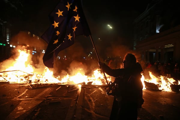 A demonstrator holds a European Union flag standing next to a burning barricade during a rally to protests against the government's decision to suspend negotiations on joining the EU in Tbilisi, Georgia, early Tuesday, Dec. 3, 2024. (AP Photo/Zurab Tsertsvadze)