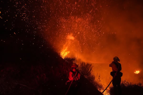 Two firefighters put out flames while battling the Franklin Fire in Malibu, Calif., Tuesday, Dec. 10, 2024. (AP Photo/Jae C. Hong)