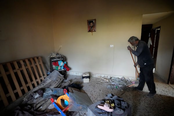 A man cleans a house, as a portrait hanging on the wall shows the late Hezbollah leader Sayyed Hassan Nasrallah, at the site where an Israeli airstrike hit a house in Aalmat village, northern Lebanon, Sunday, Nov. 10, 2024. (AP Photo/Hassan Ammar)