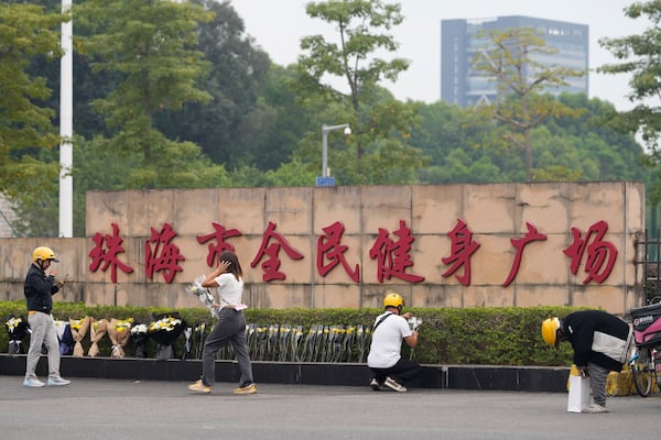 A woman walks past delivery men dropping off flowers outside the "Zhuhai People's Fitness Plaza" where a man rammed his car into people exercising at the sports center, in Zhuhai in southern China's Guangdong province on Wednesday, Nov. 13, 2024. (AP Photo/Ng Han Guan)