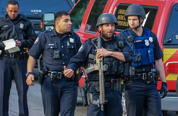 Atlanta police uniform officers bring an officer to medics to treat minor cuts after he injured himself to avoid gunfire before a six hour standoff began with the suspect being fatally shot Thursday morning, April 12, 2018 in northwest Atlanta. SWAT officers swarmed the 1400 block of Kennesaw Drive. (JOHN SPINK/JSPINK@AJC.COM)