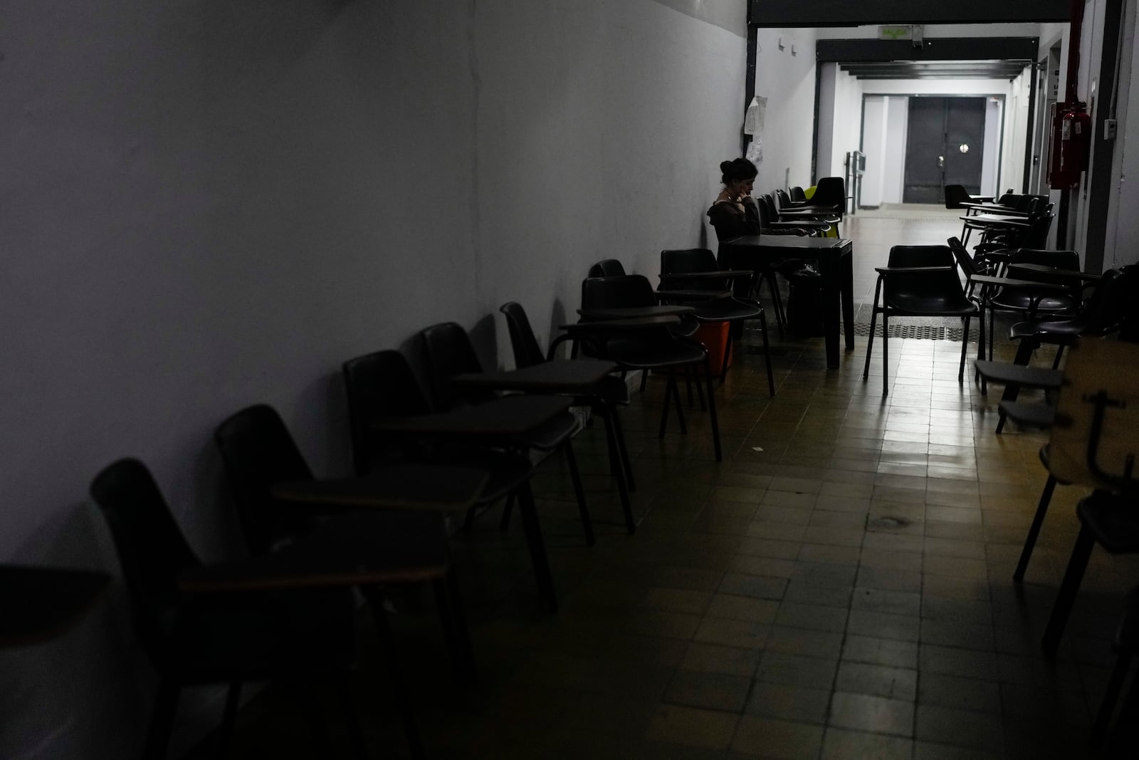 A student sits inside an empty hallway inside the Faculty of Psychology as fellow students hold class outside in the middle of a street to protest President Javier Milei's veto of higher funding for public universities, in Buenos Aires, Argentina, Wednesday, Oct. 16, 2024. (AP Photo/Natacha Pisarenko)