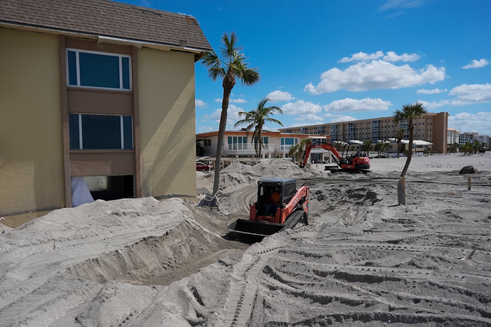 Scott Bennett, a contractor who specializes in storm recovery, drives a skid steer as he removes sand around 5 feet deep from the patio of a beachfront condominium in Venice, Fla., following the passage of Hurricane Milton, Saturday, Oct. 12, 2024. (AP Photo/Rebecca Blackwell)