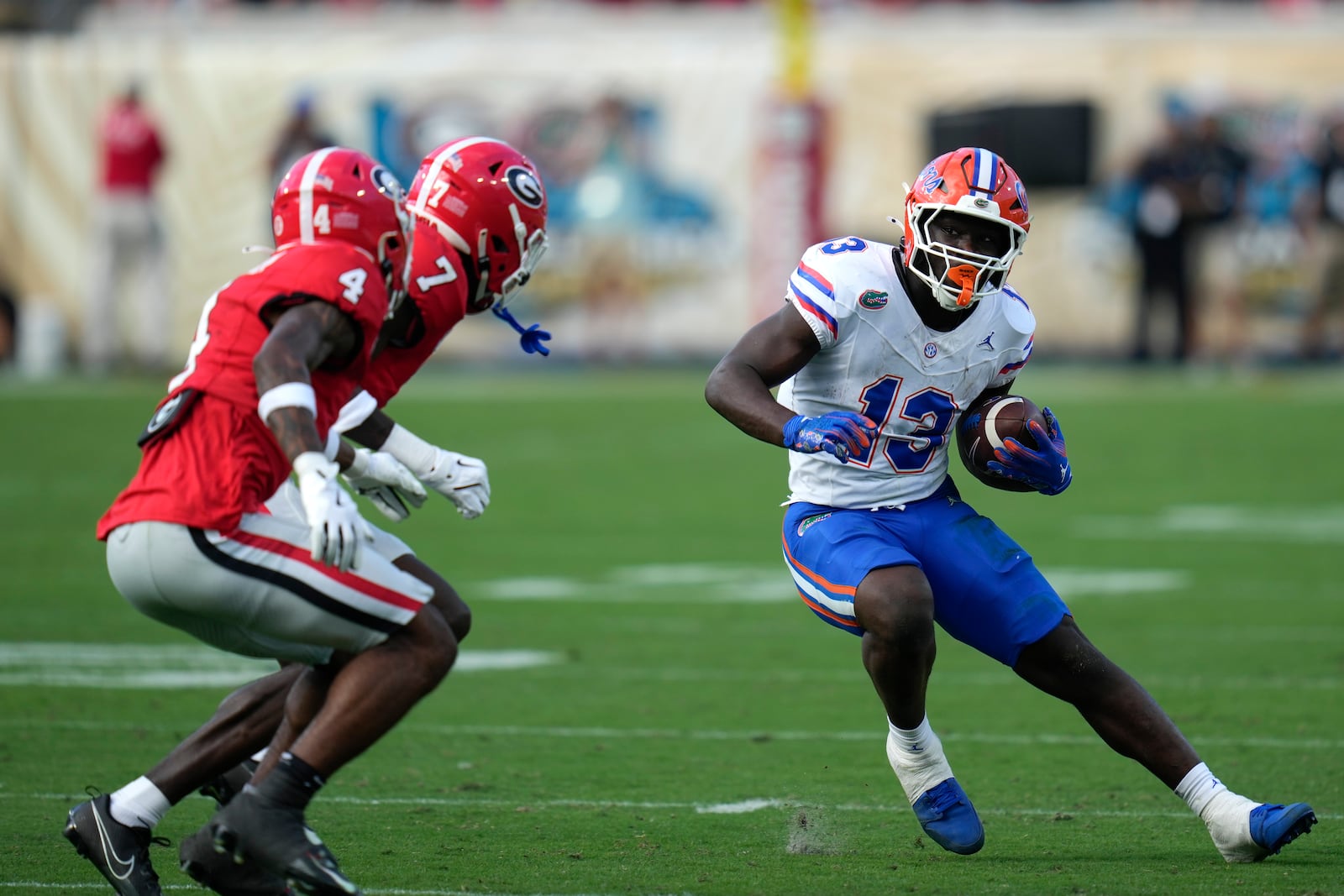 Florida running back Jadan Baugh (13) makes a move to get around Georgia defensive back KJ Bolden (4), and defensive back Daniel Harris (7) during the first half of an NCAA college football game, Saturday, Nov. 2, 2024, in Jacksonville, Fla. (AP Photo/John Raoux)