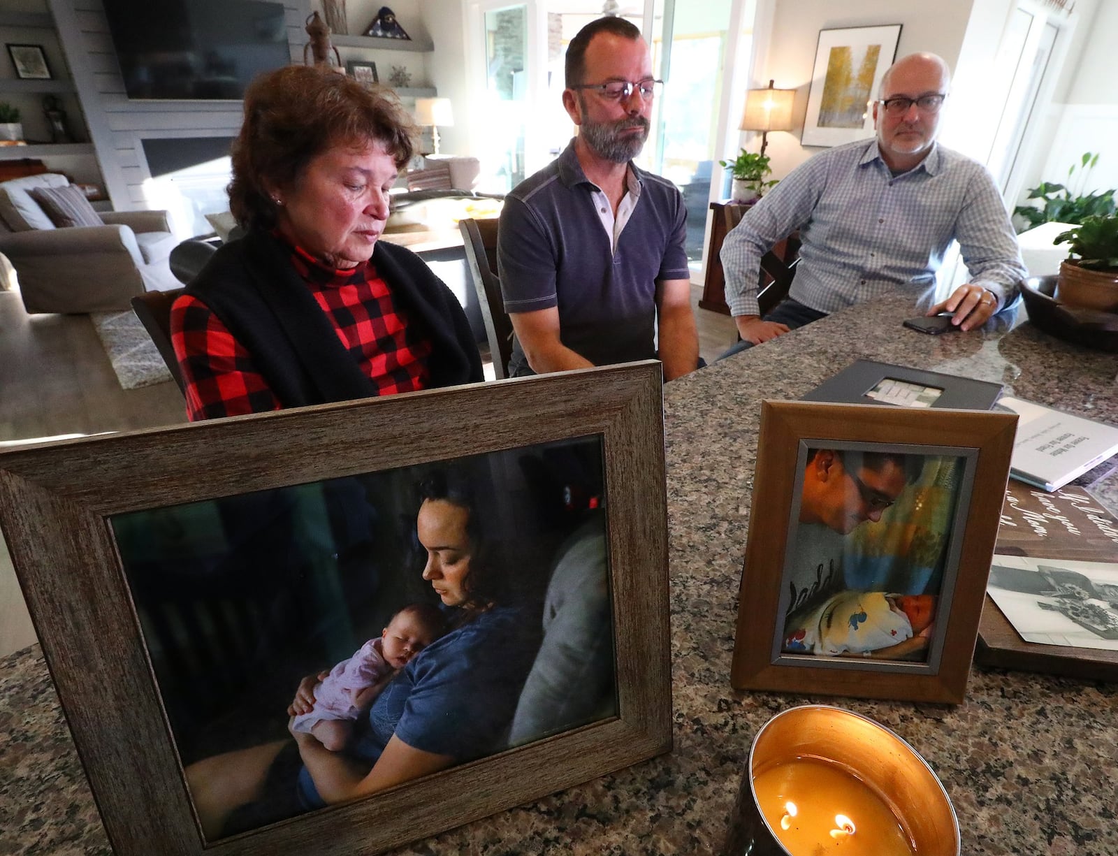 A candle burns next to a family portrait of Kaitlin Hunt and her infant, Riley, during an interview with her parents Kathy Vandiver (from left) and Gregg Vandiver and Gregg’s partner, David Lickman. Curtis Compton/ccompton@ajc.com