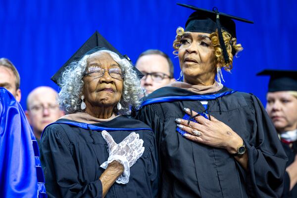 Myra Payne Elliott (left), 90, and her daughter Jocelyn Gleaton stand for the national anthem at Georgia State University’s graduation ceremony in Atlanta on Wednesday, Dec. 14, 2022. GSU presented honorary degrees to Elliott and two other Black women, now deceased, who sued to integrate the school but never enrolled. (Arvin Temkar / arvin.temkar@ajc.com)