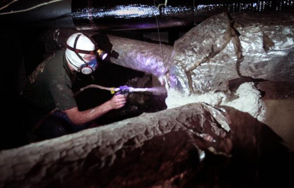 Bird-Family Insulation employee Andrew Illick spray-foams the heating, ventilation, and AC boots around the furnace to seal any holes in the crawl space in the Pennyman home.