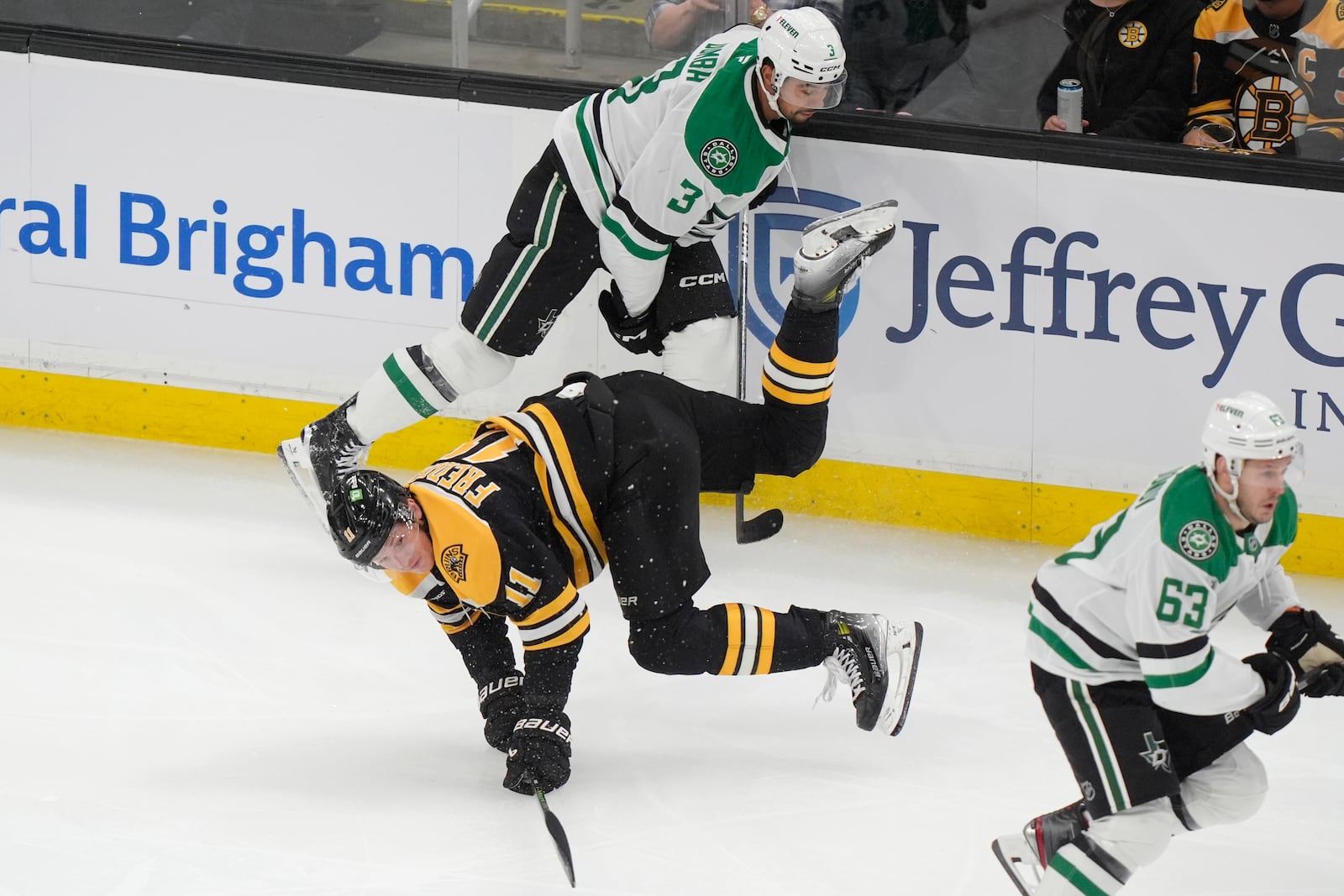 Boston Bruins center Trent Frederic (11) hits the ice as Dallas Stars defenseman Mathew Dumba (3) and right wing Evgenii Dadonov (63) vie for position in the first period of an NHL hockey game, Thursday, Oct. 24, 2024, in Boston. (AP Photo/Steven Senne)