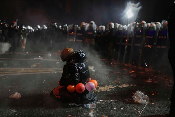 A protester sits on her knees as riot police stand guard during a protest against the arrest of Istanbul's Mayor Ekrem Imamoglu, in Istanbul, Turkey, Saturday, March 22, 2025. (AP Photo/Francisco Seco)