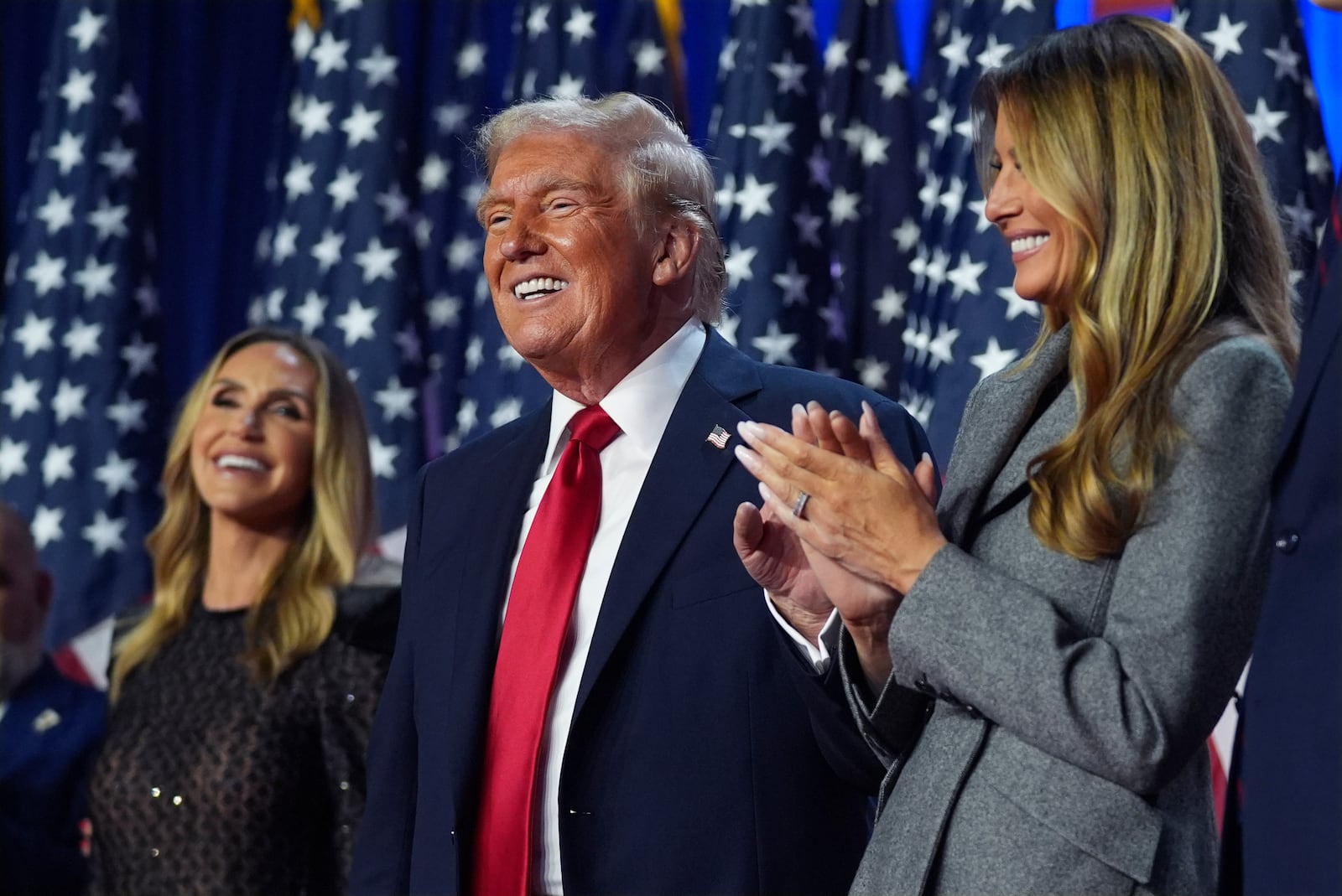 President-elect Donald Trump stands on stage with his wife Melania Trump (right) as Lara Trump watches, at an election night watch party in West Palm Beach, Fla.