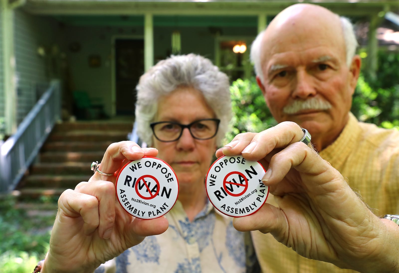 Penny and George West show off their anti-Rivian buttons outside their home near Madison. The couple says the future plant is the main issue they care about in the upcoming primary elections. (Curtis Compton / Curtis.Compton@ajc.com)