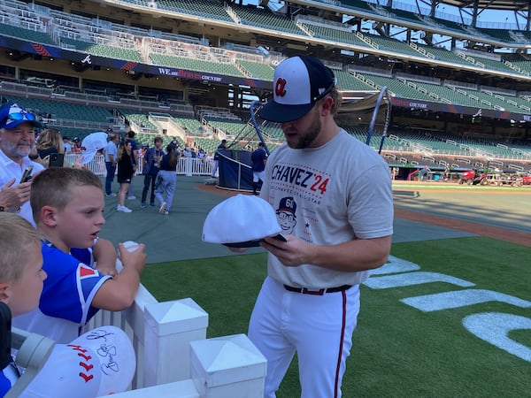 Braves reliever A.J. Minter signs an autograph prior to the team's July 2, 2024 home game vs. the San Francisco Giants while modeling a t-shirt campaigning for teammate Jesse Chavez to be selected for the All-Star Game. "His numbers speak for themselves," said Minter, who took it upon himself to print the T-shirts. (AJC photo by Ken Sugiura)