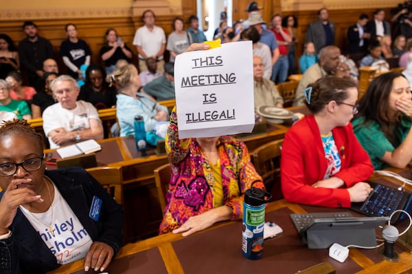 An attendee holds a sign that says “This Meeting is Illegal” during a hastily planned State Election Board meeting at the Capitol in Atlanta on Friday, July 12, 2024. (Arvin Temkar / AJC)