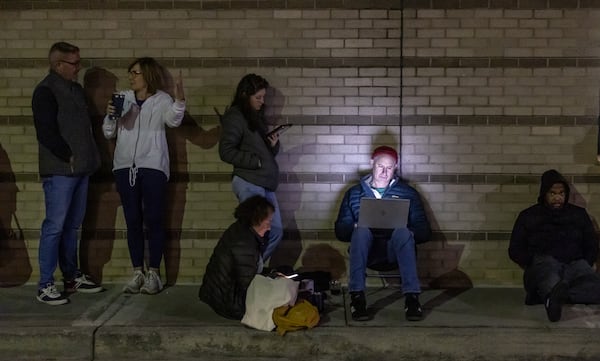 Ross Mansbach checks his laptop as he and other voters line up before the polls open Tuesday at the Joan P. Garner Library in Atlanta for the the first day of Georgia three-week early voting period. (John Spink/AJC)