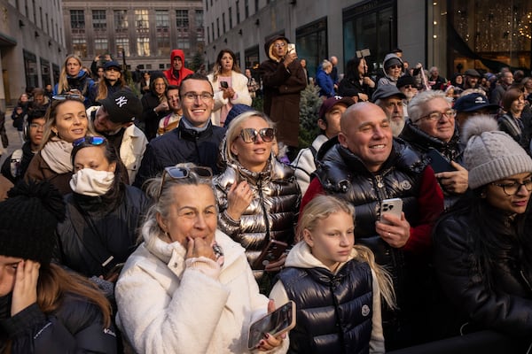 People watch the Rockefeller Center Christmas tree being lifted by a crane into place at Rockefeller Plaza, Saturday, Nov. 9, 2024, in New York. (AP Photo/Yuki Iwamura)