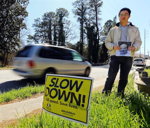 Ke Wu holds a picture of his father Jianchang Wu, who was struck and killed while trying to cross North Decatur Road in Atlanta. Ke Wu is seen here in March 2014, standing at the accident site, where a “slow down” sign had since been placed. The elder Wu and his wife were visiting their son from China. Their son believes the speed the vehicle was traveling contributed to the accident. CURTIS COMPTON / CCOMPTON@AJC.COM