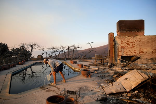 Garrett Yost gathers water from a pool while surveying his neighbors' fire-ravaged properties in the aftermath of the Palisades Fire in the Pacific Palisades neighborhood of Los Angeles, Friday, Jan. 10, 2025. (AP Photo/John Locher)