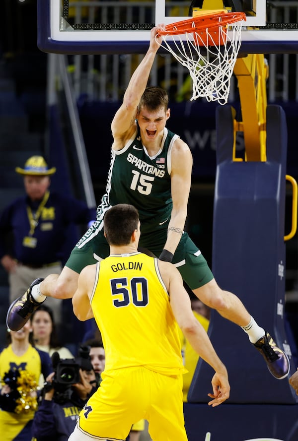 Michigan State center Carson Cooper (15) hangs from the rim after dunking against Michigan center Vladislav Goldin (50) during the second half of an NCAA college basketball game Friday, Feb. 21, 2025, in Ann Arbor, Mich. (AP Photo/Duane Burleson)