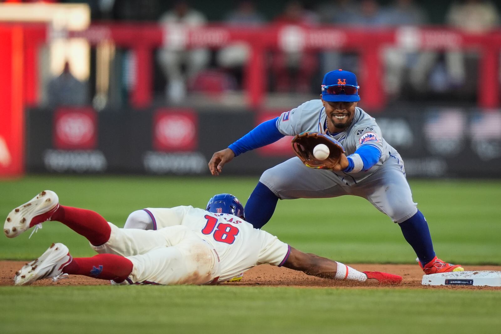 Philadelphia Phillies' Johan Rojas (18) dives safely back to second as New York Mets shortstop Francisco Lindor tries to tag him for a pickoff during the fifth inning of Game 1 of a baseball NL Division Series, Saturday, Oct. 5, 2024, in Philadelphia. (AP Photo/Chris Szagola)