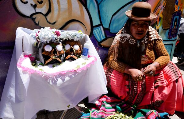 A woman sits next to her decorated human skulls at the General Cemetery as part of the annual “Ñatitas” festival, a tradition marking the end of the Catholic holiday of All Saints, in La Paz, Bolivia, Friday, Nov. 8, 2024. (AP Photo/Juan Karita)