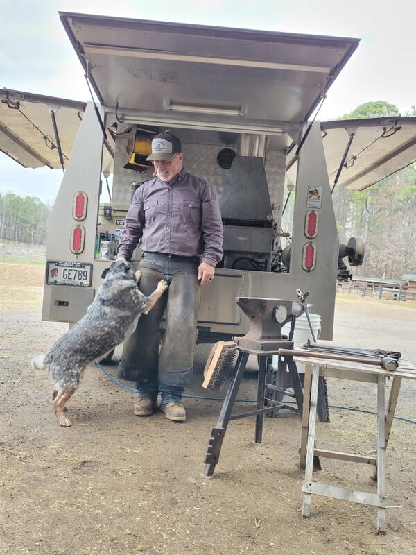 Lee Griffin, a farrier based in Ball Ground, Georgia, takes a break from shoeing horses to visit with his dog, Lena, at his work truck.