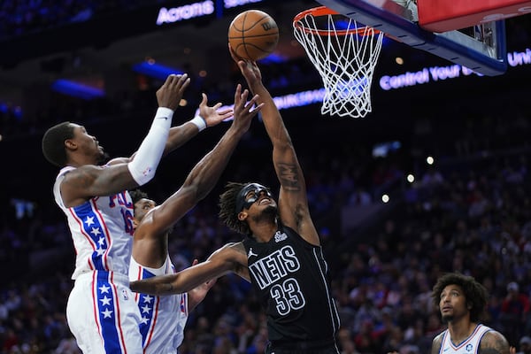 Brooklyn Nets' Nic Claxton, center, reaches for a rebound against Philadelphia 76ers' Lonnie Walker IV, left, and Joel Embiid during the first half of an NBA basketball game, Saturday, Feb. 22, 2025, in Philadelphia. (AP Photo/Matt Slocum)