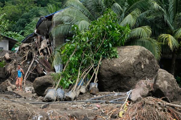 A resident passes by large boulders beside damaged homes on Saturday, Oct. 26, 2024 after being struck by a landslide triggered by Tropical Storm Trami in Talisay, Batangas province, Philippines. (AP Photo/Aaron Favila)