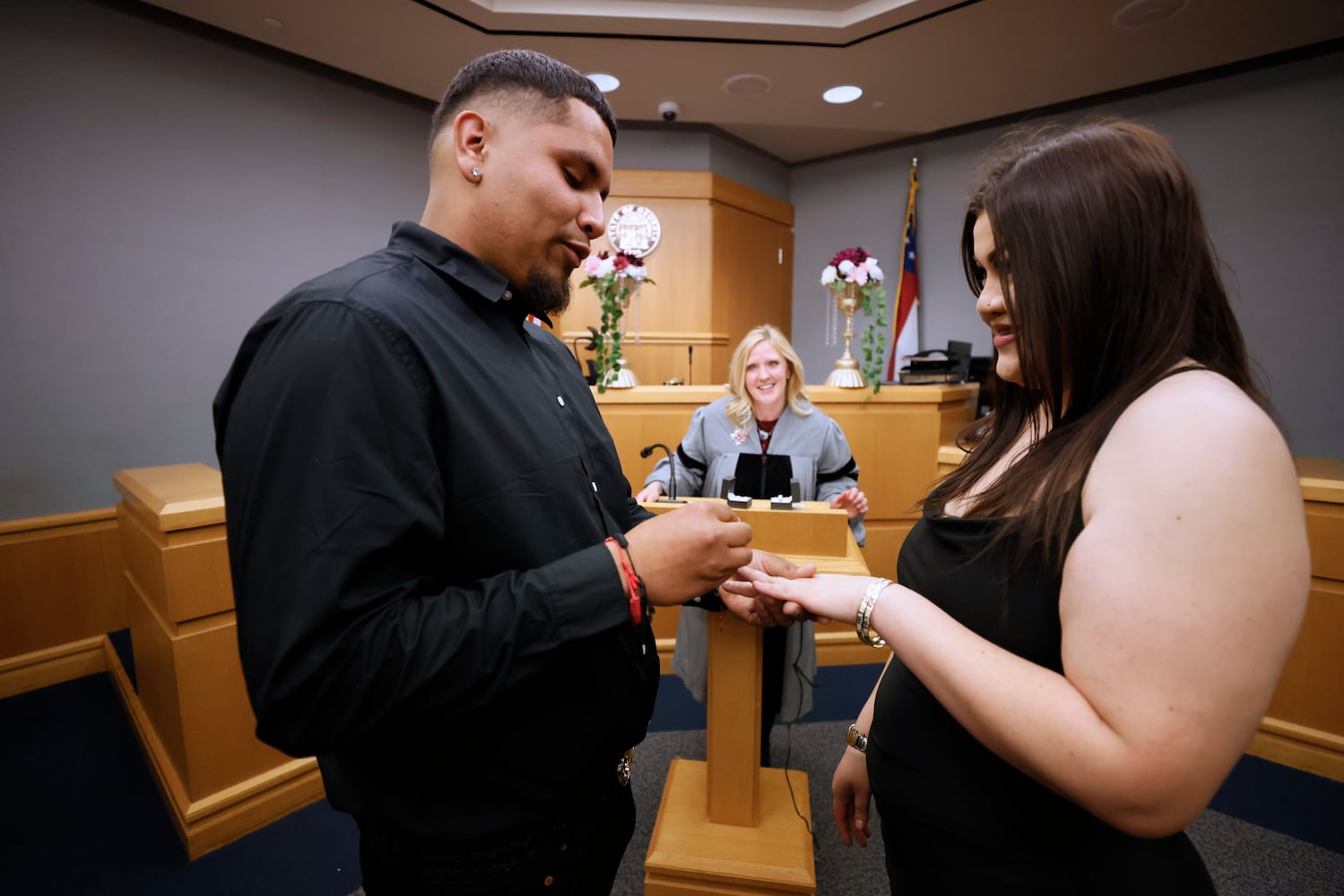 Jonathan López puts the wedding ring to Alma Escobar as Chief Magistrate Judge Kristina Hammer Blum looks in Courtroom 1C of the Gwinnett County Courthouse in Lawrenceville on Valentine’s Day, Tuesday, February 14, 2023. Miguel Martinez / miguel.martinezjimenez@ajc.com