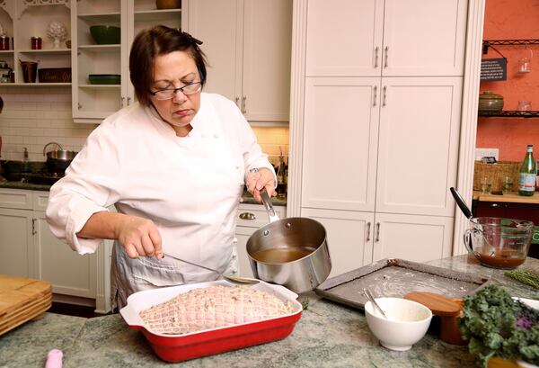 Chef Lenore Pinello pours a mix of broth and wine into the roasting pan as she prepares a turkey breast at her cooking space, In The Kitchen, in Tequesta.  