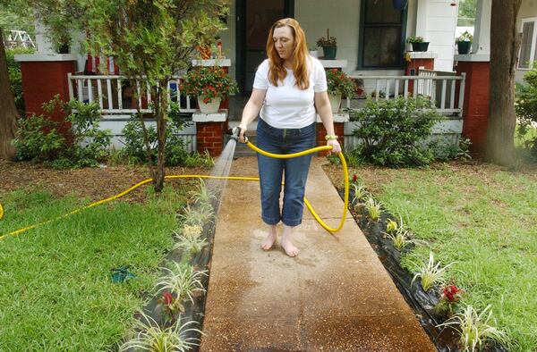 Elaine Hubbart waters her plants. She has put plastic down in the beds to ward off the birds. On the burning issue that divides the town, she's of the anti-chicken persuasion. (Kimberly Smith/AJC file)